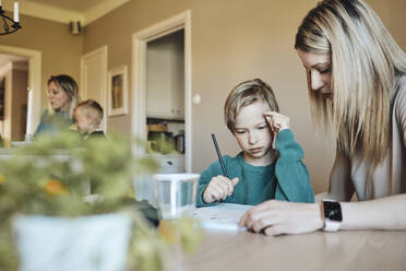 Blond woman assisting son with homework at home - MASF33516
