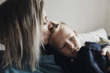 Mutter küsst Sohn, der zu Hause auf dem Sofa sitzt - MASF33522