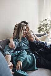 Lesbian mothers sitting with sons on sofa at home - MASF33524