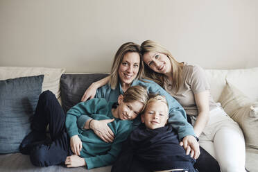 Porträt von lesbischen Müttern mit Söhnen, die zusammen auf dem Sofa zu Hause sitzen - MASF33525