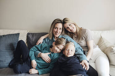 Portrait of lesbian mothers with sons sitting together on sofa at home - MASF33525