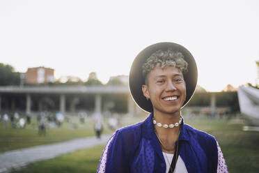 Portrait of happy young man with curly hair wearing hat at park - MASF33581