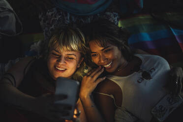 Happy non-binary person taking selfie with female friend through smart phone - MASF33614