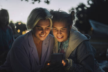 Glückliche nicht-binäre Person, die ihr Smartphone mit einer Freundin bei Sonnenuntergang teilt - MASF33615