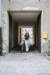 Frau, die mit dem Fahrrad aus einem Archivportal tritt - MASF33627