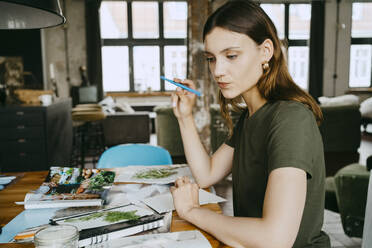 Nachdenkliche Food-Stylistin, die bei der Arbeit im Studio die Lippen schürzt und einen Stift hält - MASF33653