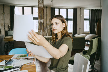 Junge Unternehmerin vergleicht Fotos am Tisch im Atelier - MASF33657