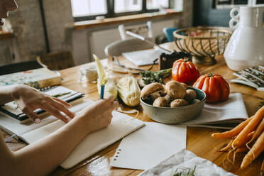 Hand einer Foodstylistin, die neben frischem Gemüse auf einem Tisch im Studio Tagebuch schreibt - MASF33671