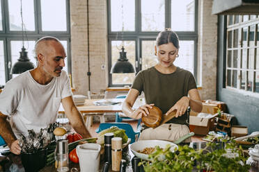 Male colleague looking at female chef preparing food in studio - MASF33678