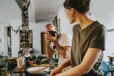 Männlicher Fotograf, der eine Köchin beim Kochen im Studio fotografiert - MASF33682