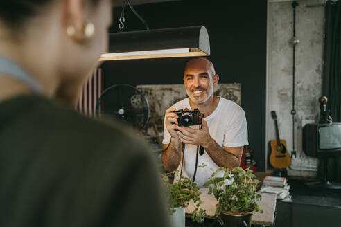 Glücklicher männlicher Fotograf, der eine Digitalkamera hält und einen Kollegen im Studio betrachtet - MASF33686