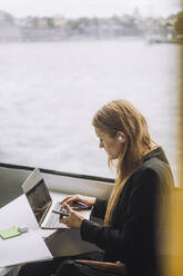Seitenansicht einer Freiberuflerin, die einen Laptop benutzt, während sie in einer Fähre sitzt - MASF33702