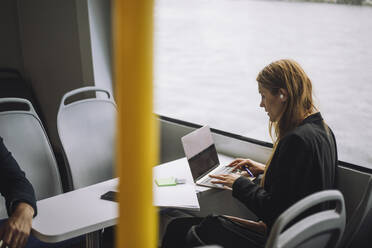 Female entrepreneur typing on laptop while sitting in ferry - MASF33703