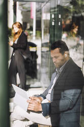 Geschäftsmann, der einen Laptop benutzt, während er an einer Bushaltestelle in der Sonne sitzt - MASF33711