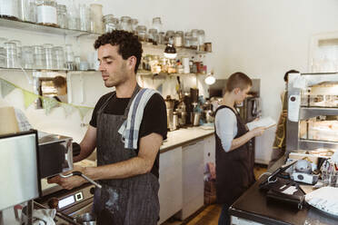 Male barista preparing coffee using coffee maker in cafe - MASF33728