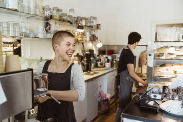 Junge glückliche Besitzerin schaut weg, während sie in einem Café Kaffee zubereitet - MASF33731