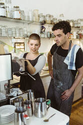Weibliche und männliche Besitzer lernen den Umgang mit der Kaffeemaschine im Café - MASF33732