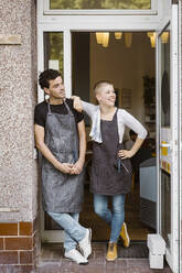 Männliche und weibliche Besitzer schauen weg, während sie am Eingang eines Cafés stehen - MASF33738