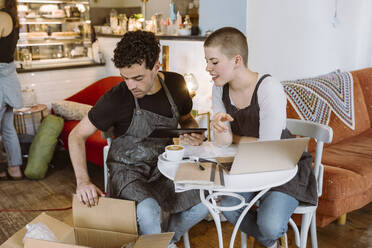 Männliche und weibliche Besitzer, die auf einem Stuhl in einem Café sitzen und eine Box überprüfen - MASF33742