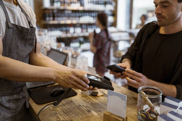 Mittelteil eines männlichen Inhabers, der einem Kunden, der in einem Geschäft eine Online-Zahlung vornimmt, eine Kreditkartenmaschine gibt - MASF33767
