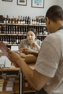 Männlicher Inhaber zeigt einer Kollegin im Weinladen das Inventar - MASF33775