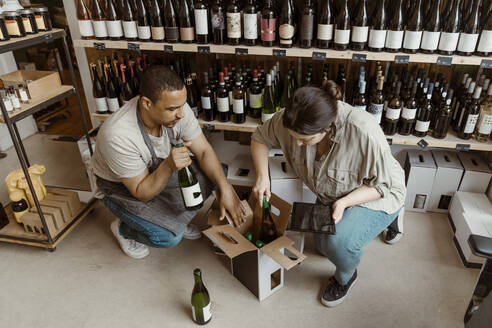 Männliche und weibliche Geschäftsinhaber, die in einem Weinladen Flaschen aus dem Karton nehmen - MASF33777