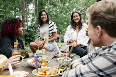 Lächelnde Frauen im Gespräch mit Freunden mit Essen auf dem Tisch während einer Gartenparty im Hinterhof - MASF33813