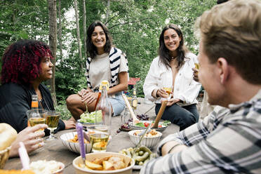 Smiling women talking to friends with food on table during garden party in back yard - MASF33813