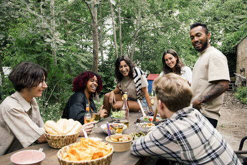 Glückliche männliche und weibliche Freunde, die sich beim Essen während einer Gartenparty im Hinterhof vergnügen - MASF33814