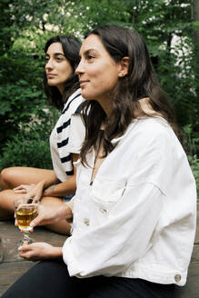 Lächelnde Frau hält ein Glas, während sie mit einer Freundin auf einer Party sitzt - MASF33815