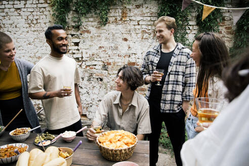 Männliche und weibliche Freunde unterhalten sich bei einer Gartenparty im Hinterhof mit einem Glas in der Hand - MASF33817