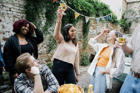 Fröhliche Frau, die mit männlichen und weiblichen Freunden bei einer Dinnerparty im Hinterhof feiert - MASF33820