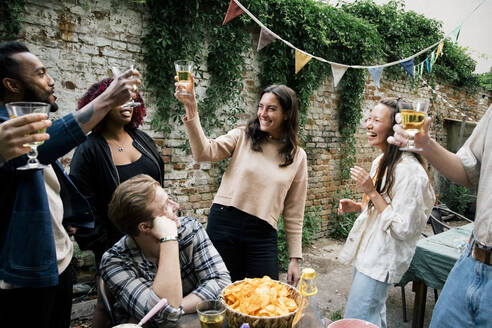 Multirassische männliche und weibliche Freunde stoßen mit Getränken an, während sie auf einer Dinnerparty im Hinterhof feiern - MASF33821