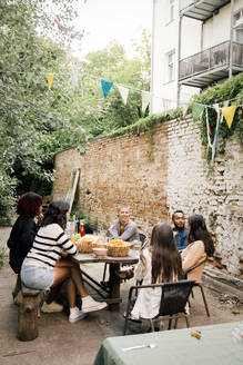 Männliche und weibliche Freunde kommunizieren miteinander bei einer Dinnerparty im Hinterhof - MASF33827