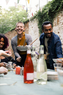 Smiling man and woman serving food to friends at dining table during party in back yard - MASF33830