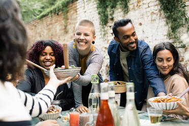 Young woman with toothy smile passing bowl to friend at dinner party - MASF33832