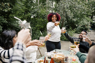 Young woman toasting drinks with multiracial friends during dinner party in back yard - MASF33856