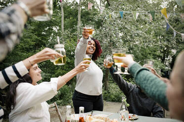 Cheerful friends celebrating while toasting drinks with each other during dinner party - MASF33857