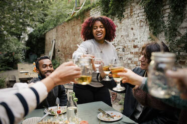 Woman with curly hair toasting drinks with friends during social gathering in back yard - MASF33858