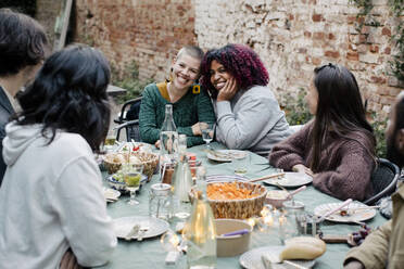 Freunde unterhalten sich mit multirassischen Frauen, die am Esstisch sitzen, während einer Dinnerparty im Hinterhof - MASF33864