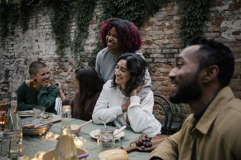 Lächelnde multirassische männliche und weibliche Freunde, die sich während einer Dinnerparty miteinander unterhalten - MASF33873