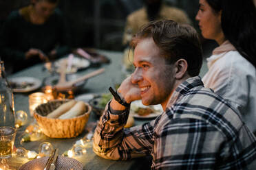 Side view of smiling young man leaning on elbow at dining table during sinner party - MASF33880