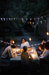 Friends enjoying dinner party in back yard decorated with bunting - MASF33884