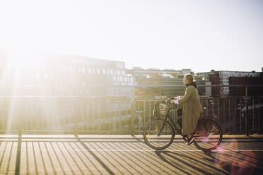 Seitenansicht einer weiblichen Geschäftsfrau, die an einem sonnigen Tag auf der Straße Fahrrad fährt - MASF33888
