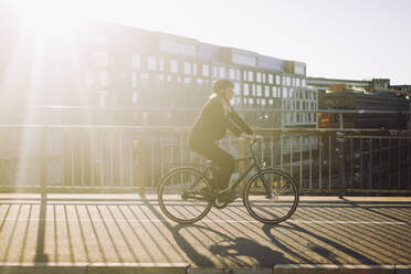 Businesswoman commuting through bicycle on road during sunny day - MASF33889