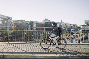Businessman riding bicycle on cycling path against buildings in city - MASF33893