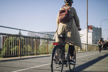 Rückansicht einer Geschäftsfrau mit Rucksack auf einem Fahrrad auf der Fahrbahn - MASF33896