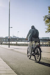 Geschäftsmann fährt Fahrrad auf der Fahrbahn an einem sonnigen Tag - MASF33899