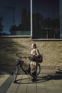 Geschäftsfrau mit Fahrrad vor einer Wand stehend - MASF33900