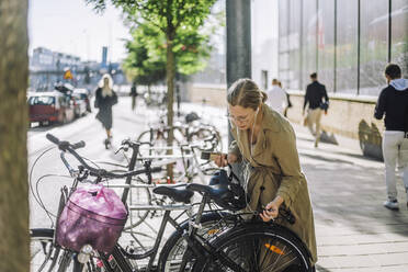 Businesswoman listening music while standing near bicycle at parking station - MASF33902